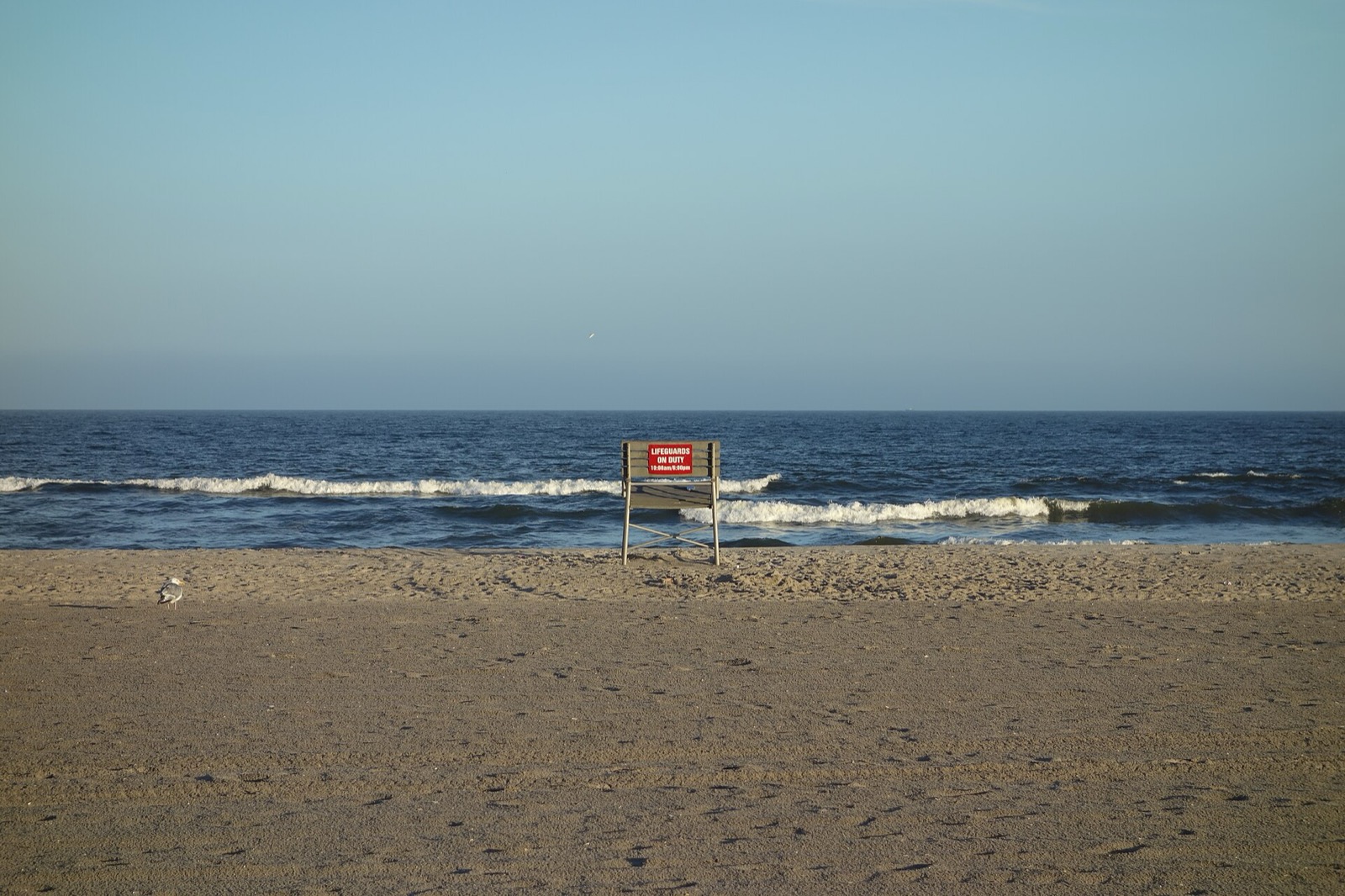 An empty lifeguard chair with a red sign on a sandy beach facing the ocean