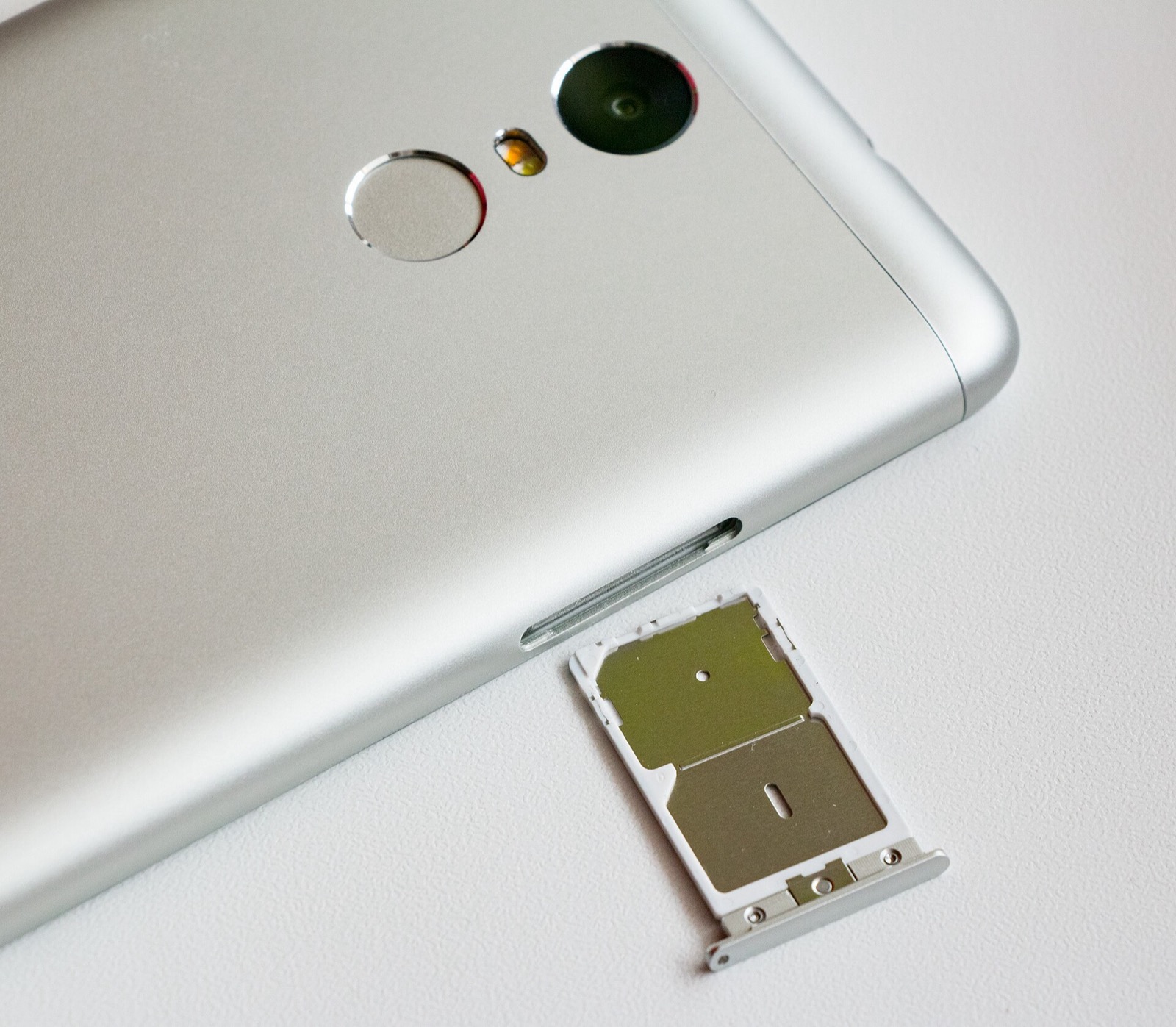 Silver smartphone next to its open dual SIM card tray