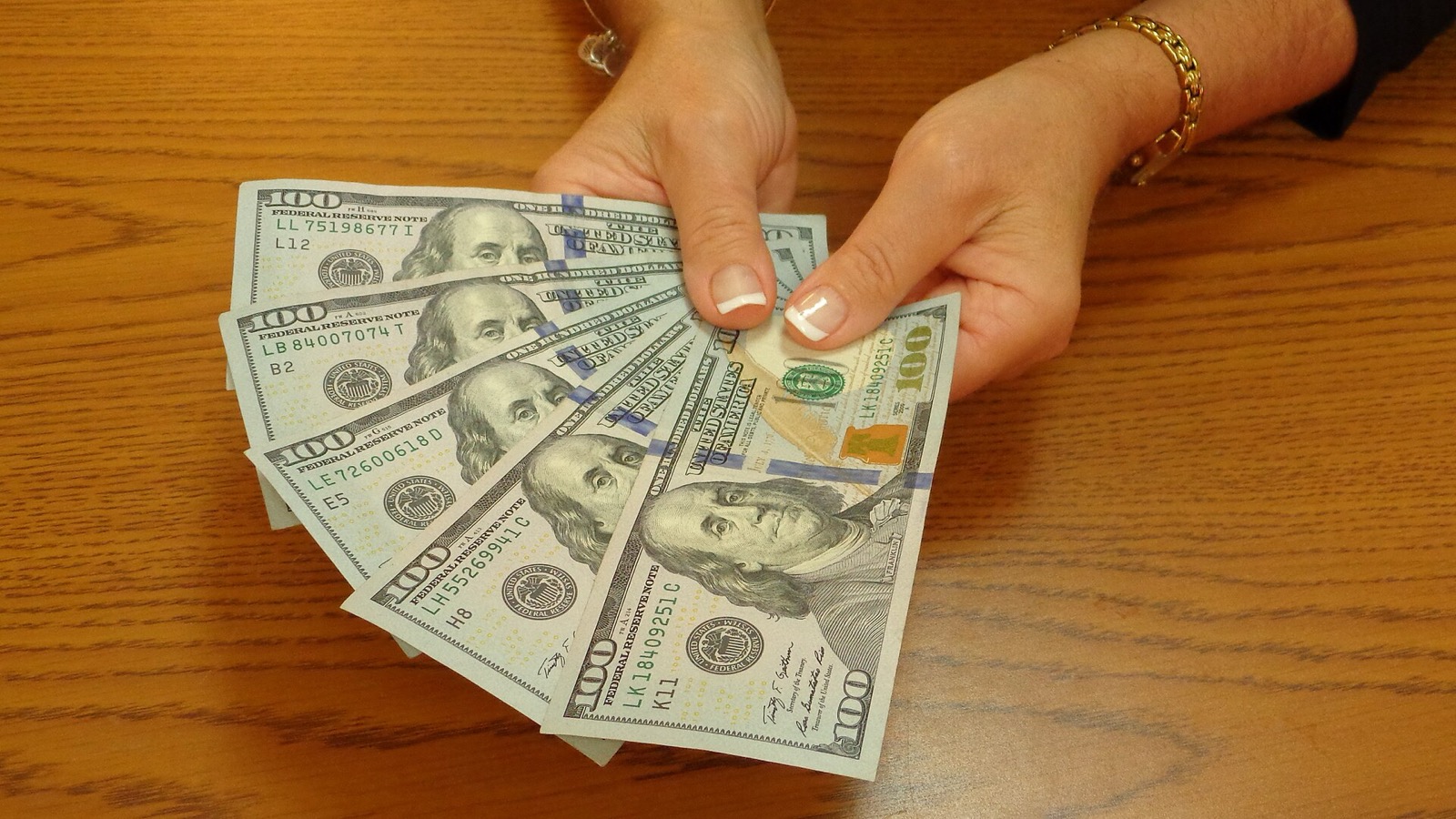 Hands holding a fan of five $100 bills